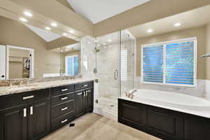 Beautifully updated master bathroom with tile floor, walk-in shower, a garden tub, lofted ceiling, and double vanity