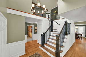 Stairway featuring a chandelier, ornamental molding, hardwood  floors, a wainscoted wall, and a towering ceiling