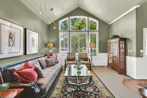 Carpeted living room with lofted ceiling, wainscoting, a decorative wall, and a textured ceiling