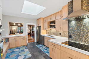 Kitchen featuring light brown cabinets, wall chimney exhaust hood, appliances with stainless steel finishes, and a sink