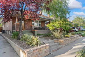 View of property hidden behind natural elements with brick siding, covered porch, central air condition unit, and a chimney