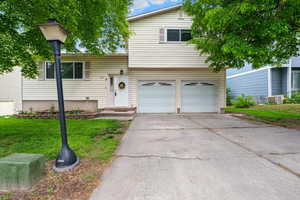 View of front of house with a garage, a front yard, driveway, and central AC