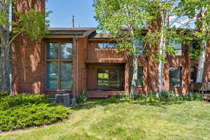 Back of house with cooling unit, a lawn, a chimney, and a balcony