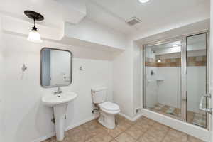 Bathroom featuring a stall shower, toilet, baseboards, a sink, and tile patterned flooring