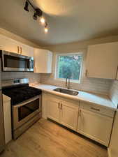 Kitchen with appliances with stainless steel finishes, a sink, light countertops, white cabinetry, and a textured ceiling