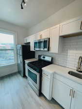 Kitchen with stainless steel appliances, a sink, light countertops, white cabinets, and a textured ceiling