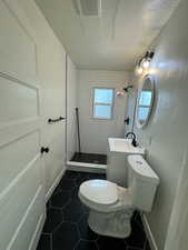 Full bath with tiled shower, tile patterned floors, toilet, a sink, and a textured ceiling