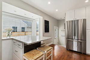 Kitchen featuring freestanding refrigerator, wood flooring, light stone countertops, and white cabinets