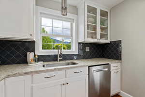 Kitchen featuring dishwasher, a sink, glass insert cabinets, white cabinets, and tasteful backsplash
