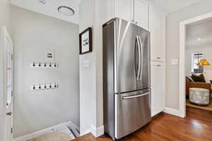 Kitchen with freestanding stainless refrigerator, wood floors, white cabinetry.