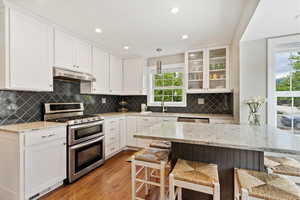 Kitchen with appliances with stainless steel finishes, under cabinet range hood, a sink, a breakfast bar, and light wood floors