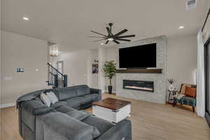 Living room with light wood-type flooring, ceiling fan, a stone fireplace, stairway, and recessed lighting