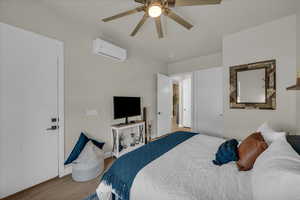 Bedroom with a wall mounted AC, wood finished floors, a ceiling fan, and baseboards