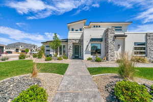 Modern home with stucco siding, stone siding, a front yard, and a residential view