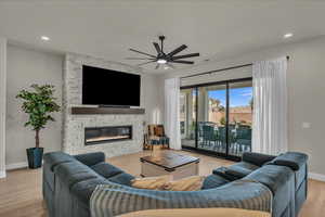Living room with a ceiling fan, baseboards, a stone fireplace, wood finished floors, and recessed lighting