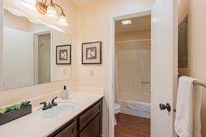 Bathroom with vanity, toilet, wood finished floors, and shower / tub combo