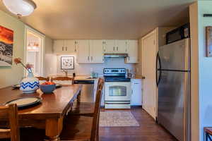 Kitchen with appliances with stainless steel finishes, dark wood finished floors, under cabinet range hood, white cabinets, and light countertops
