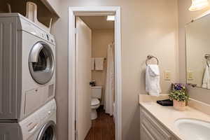Full bath featuring stacked washer / drying machine, vanity, wood finished floors, toilet, and a shower with curtain