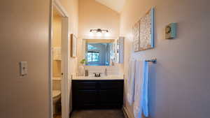 Bathroom with toilet, vanity, lofted ceiling, a baseboard radiator, and a textured wall