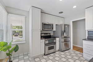 Kitchen with stainless steel appliances, dark countertops, white cabinets, and recessed lighting