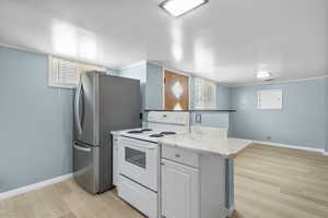 Kitchen featuring white electric range, freestanding refrigerator, light wood finished floors, and baseboards