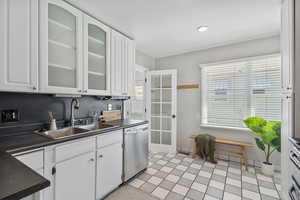 Kitchen featuring stainless steel dishwasher, a sink, dark countertops, white cabinetry, and recessed lighting