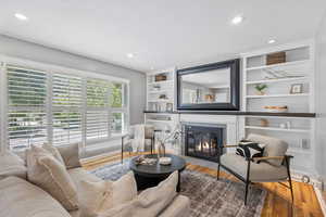 Living area featuring a fireplace with flush hearth, wood finished floors, recessed lighting, and built in shelves
