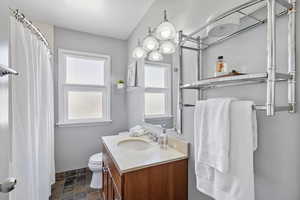 Bathroom featuring stone tile flooring, vanity, toilet, curtained shower, and baseboards