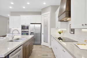 Kitchen featuring appliances with stainless steel finishes, a sink, custom range hood, white cabinets, and recessed lighting
