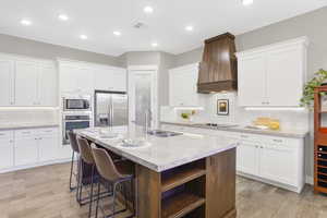 Kitchen featuring stainless steel appliances, a sink, custom range hood, open shelves, and tasteful backsplash