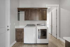Laundry room featuring cabinet space, washer and clothes dryer, baseboards, and light wood-style flooring