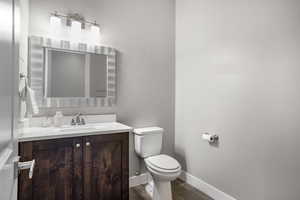 Half bath featuring toilet, vanity, wood finished floors, and baseboards