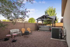 Fenced backyard featuring central air condition unit, a hot tub, and a gazebo
