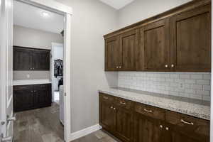 Kitchen with dark wood-style flooring, decorative backsplash, dark brown cabinets, and light stone counters