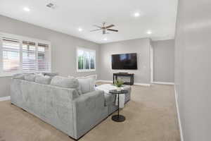 Living room featuring light colored carpet, baseboards, ceiling fan, and recessed lighting