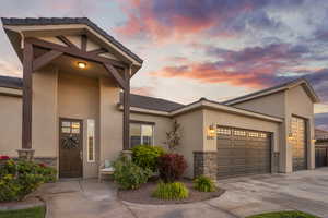 View of front facade with stone siding, an attached garage, concrete driveway, and stucco siding