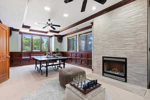 Dining area featuring ceiling fan, crown molding, a decorative wall, carpet, and a tiled fireplace
