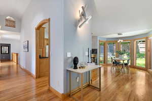 Corridor featuring light wood finished floors, baseboards, a chandelier, high vaulted ceiling, and arched walkways