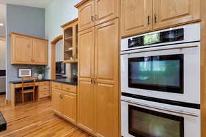 Kitchen featuring double oven, light wood finished floors, light brown cabinets, and glass insert cabinets