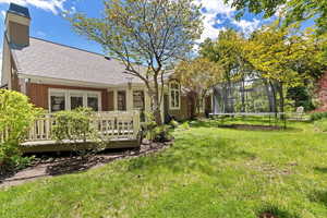 View of grassy yard featuring a trampoline and a wooden deck