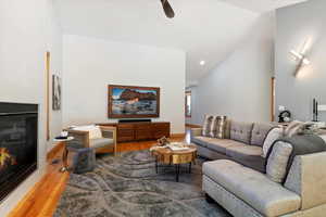 Living room with vaulted ceiling, a tile fireplace, light wood-type flooring, a ceiling fan, and recessed lighting