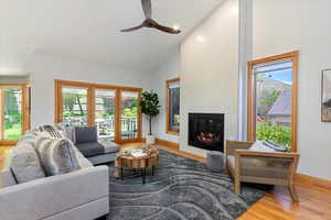 Living room featuring wood finished floors, high vaulted ceiling, french doors, ceiling fan, and a large fireplace
