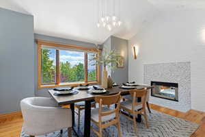 Dining space featuring vaulted ceiling, wood finished floors, a fireplace, and a chandelier