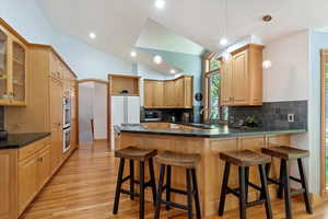 Kitchen featuring a peninsula, a sink, light wood-style flooring, backsplash, and lofted ceiling