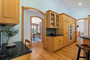 Kitchen featuring arched walkways, light wood-style flooring, double oven, glass insert cabinets, and tasteful backsplash