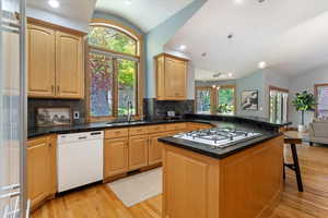 Kitchen with white dishwasher, vaulted ceiling, a sink, stainless steel gas stovetop, and light wood finished floors