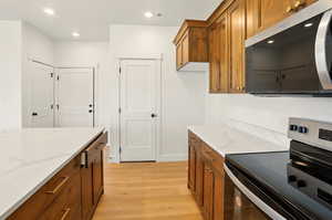 Kitchen with stainless steel appliances, brown cabinetry, light wood finished floors, light stone counters, and recessed lighting