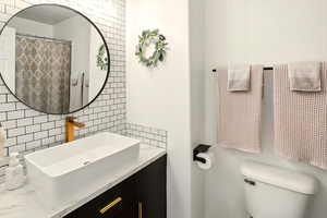 Bathroom with tile walls, toilet, vanity, and decorative backsplash
