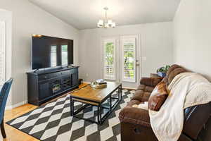 Living room with vaulted ceiling, a chandelier, wood finished floors, and baseboards