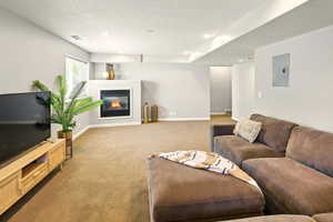 Carpeted living room with electric panel, baseboards, a glass covered fireplace, and recessed lighting